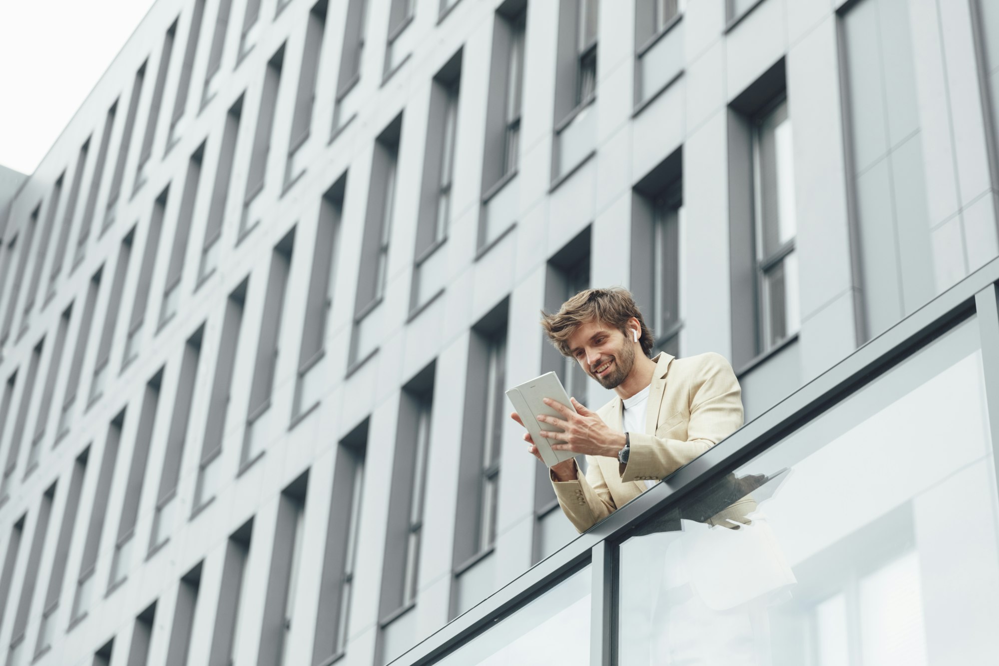 Man standing on balcony of office building with tablet